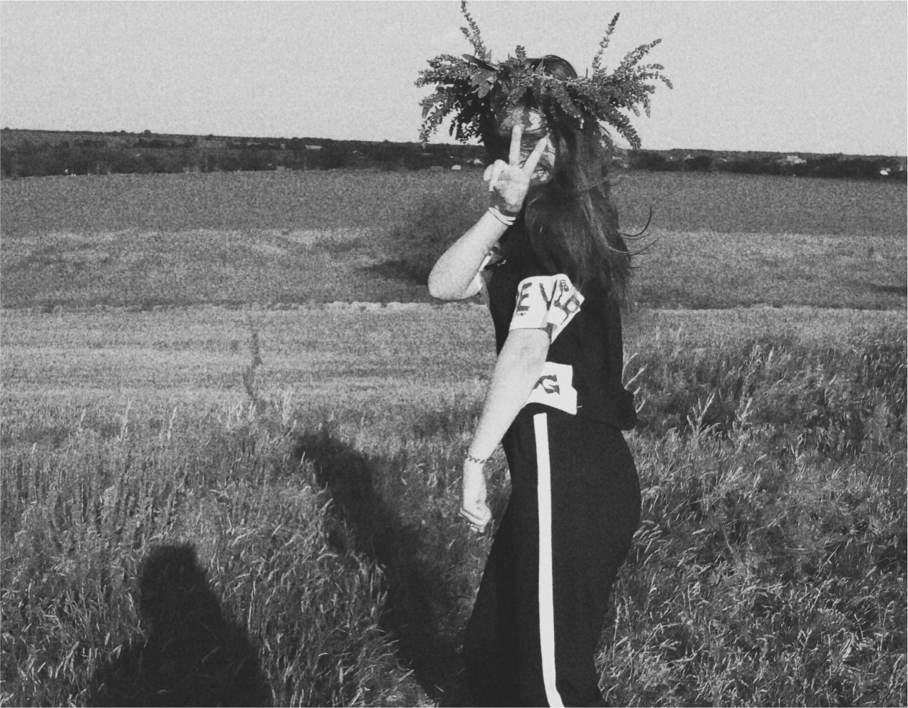Mädchen im Feld, das eine Krone aus Blättern trägt und ein Friedenszeichen zeigt, Schwarz-Weiß-Foto.