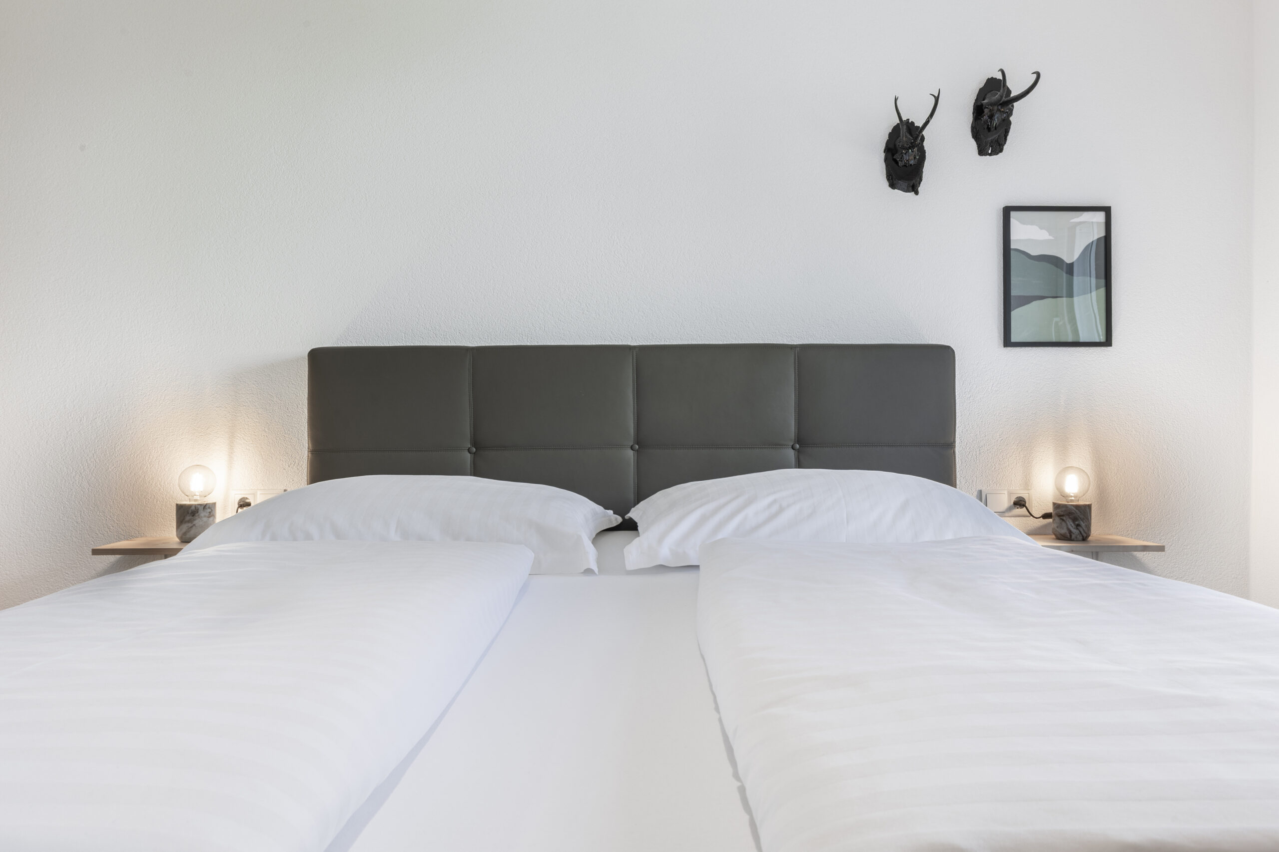 Minimalistisch eingerichtetes Schlafzimmer mit einem Doppelbett, zwei Wandleuchten und schlichten Wanddekorationen.